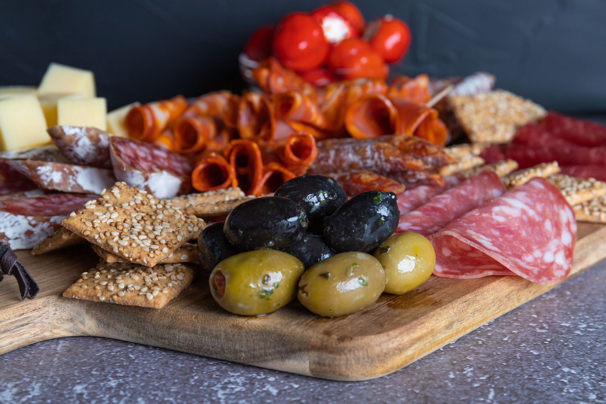 Cutting board with prosciutto, salami, cheese,bread sticks and olives on dark stone background. From top view
